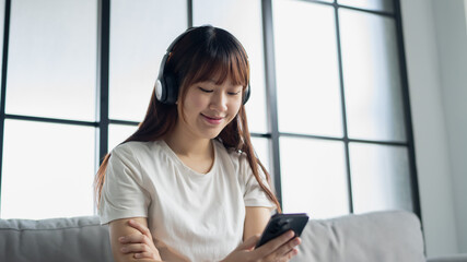 Obraz premium Asian woman wearing headphone listen to music and using smartphone choose playlist