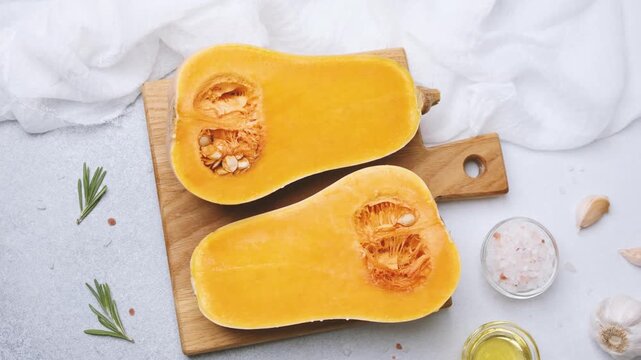 Butternut squash halves on wooden board with rosemary garlic salt and olive oil