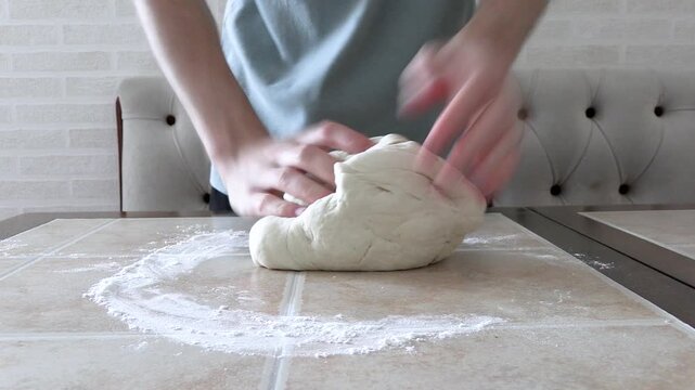 A young man kneads the dough with his hands on the table. Close-up of kneading dough with only hands in the frame