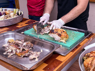 Cook slicing roasted chicken on a cutting board in a kitchen setting. Culinary preparation, food service, and gastronomy.