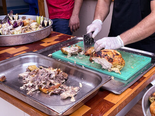 Cook slicing roasted chicken on a cutting board in a kitchen setting. Culinary preparation, food service, and gastronomy.