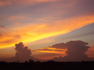 A dramatic sunset paints the sky with fiery orange and yellow hues over a silhouetted landscape with towering storm clouds.