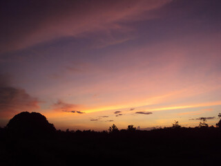 A breathtaking sunset paints the sky in vibrant shades of purple, pink, and orange above a dark, silhouetted landscape.