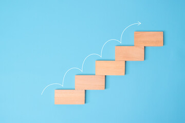 Wooden block stacking as step stair with white arrow up on blue background, Ladder of success in business growth concept