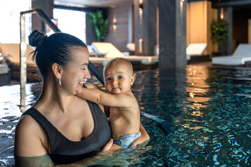 Mother with baby in warm spa pool. Family relaxation in water.
