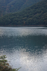 Light shines on a blue lake below a mountain full of trees.