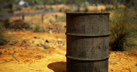 Naklejka premium A rusty, weathered barrel stands alone in a parched, rugged terrain. Surrounding grasses dry under the afternoon sun, hinting at a stark wilderness untouched by time.