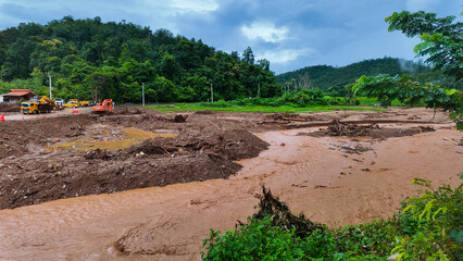 A muddy river flood aftermath with debris and heavy machinery working on recovery efforts.