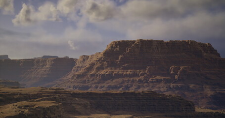 Majestic mountains rise sharply against a backdrop of a cloudy sky. Golden desert terrain stretches out, showcasing the unique geological formations and vast beauty of the landscape.