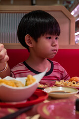 Young Asian boy tasting sushi rolls in a cozy restaurant setting, dining with joy and appetite