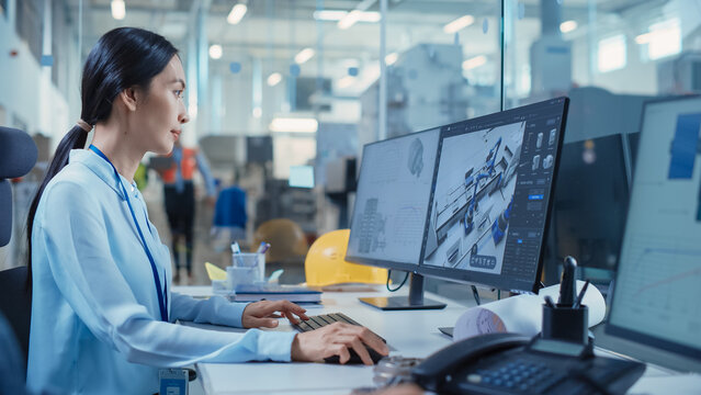 High-tech Factory: Asian Female Engineer Uses 3d Cad Software on Dual Monitors, Designing Automated Production Line. Modern Industrial Product Development. Screen Show Setup of Robot Arm Assembly Line