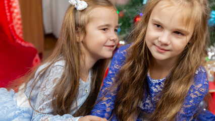 A happy little girls in a beautiful blue dress sitting in festive Christmas interior with a gifts and cheerful laughing.