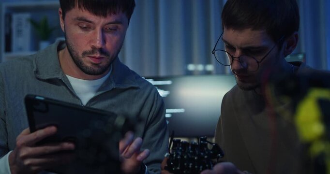Team adult male engineer collaborate on robotic hand project using AI code solutions machine learning at tech workspace night. Artificial intelligence interface, collaboration prototype development.