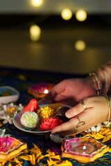 Diwali celebration. Hands holding decorative sweets and flowers for festive rituals.