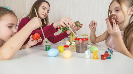 Mother and her daughter painting eggs. Happy family preparing for Easter. Cute little child girl wearing bunny ears.