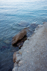 Close-up view of rocky coastline with transparent turquoise sea water. The photo captures the clarity of the waves gently covering the stones, creating a peaceful and refreshing seaside atmosphere.