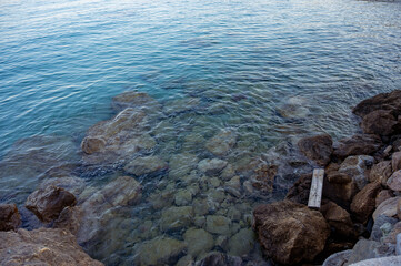 Close-up view of rocky coastline with transparent turquoise sea water. The photo captures the clarity of the waves gently covering the stones, creating a peaceful and refreshing seaside atmosphere.