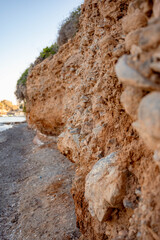 Close-up view of a rugged coastal cliff with textured layers of rock and soil, shaped by natural erosion over time. The image captures the raw beauty of nature and the power of geological 