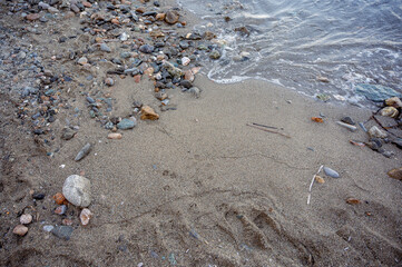 Smooth pebbles and stones scattered along the sandy beach with gentle sea waves touching the shore.