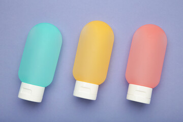 Travel bottles with body care cosmetics on purple background