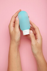 Hand holding plastic tube for travel on pink background. Cosmetic beauty product branding mockup. Vertical photo