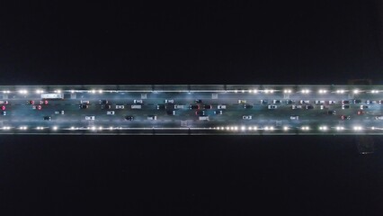 Bridge over the river with the traffic at night. Top Down Aerial Drone view of a road at night with cars driving, headlights reflecting.