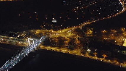Aerial shot of glowing Budapest with bright bridge across dark river in night time, Hungary