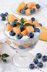 Glass bowl with yogurt, melon, blueberries, mint on a light table.Selective focus.
