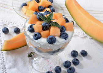 Glass bowl with yogurt, melon, blueberries, mint on a light table.Selective focus.