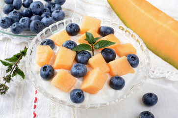 Glass bowl with yogurt, melon, blueberries, mint on a light table.Selective focus.