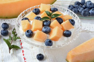 Glass bowl with yogurt, melon, blueberries, mint on a light table.Selective focus.