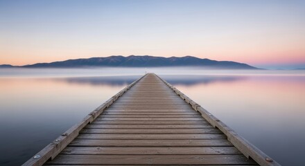 Obraz premium Serene lakeside sunrise with wooden pier leading to misty mountains