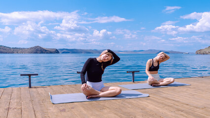 Yoga practice on a sunny dock by the serene lake with two women enjoying wellness
