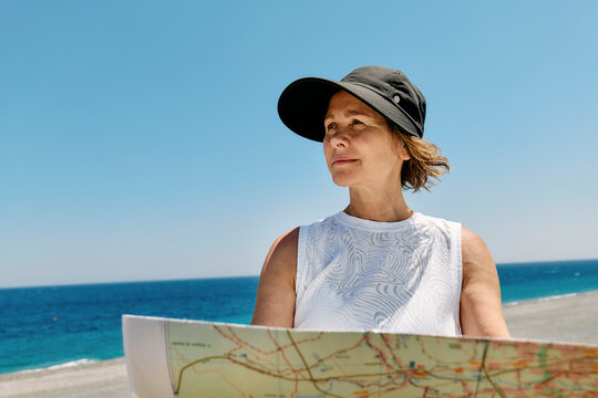 Woman looking at map by the sea wearing hat on summer day outdoors