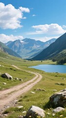 Winding dirt path leading to a serene mountain lake surrounded by lush greenery and towering peaks under a bright blue sky.