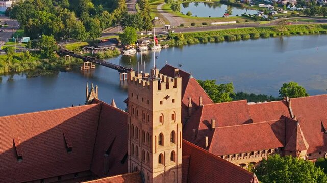 Cinematic orbit of Malbork Castle tower Polish flag waving above Nogat river