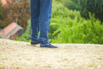 Close view of man in jeans strolling on hill in park. Shoes on dry grass. Concept of leisure,...