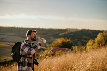 Fototapeta premium Photographer drinking water in a field during golden hour