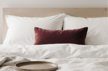 Obraz premium White pillow, white bedding, burgundy cushion, wooden headboard, and cozy blanket create serene, inviting bedroom atmosphere with soft natural light and minimalistic style