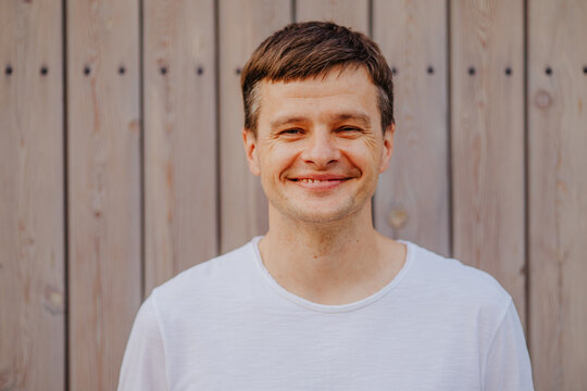 Smiling person in white shirt standing outdoors against wooden background