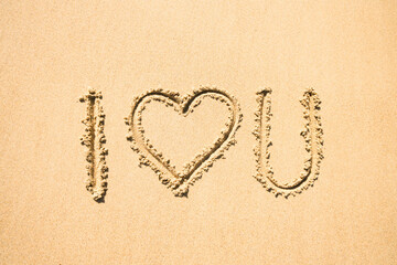 I love you. Text with a heart written in the golden sand.
