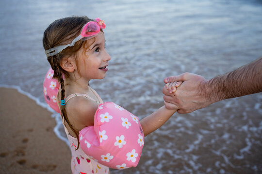 Child with swim float holding parent's hand at the beach