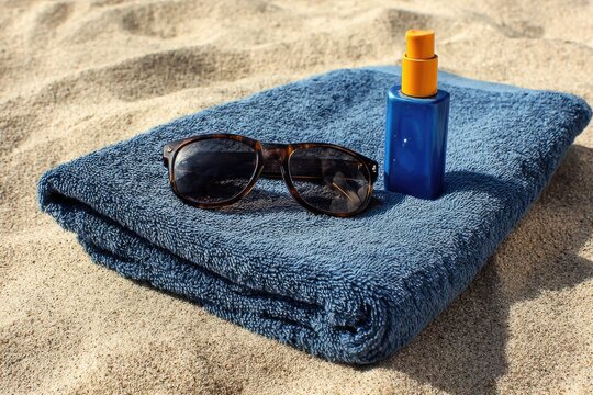 Blue towel, sunglasses, and sunscreen on sand