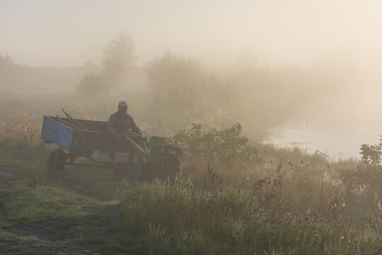 A man rides a motoblock on a foggy morning in the meadows