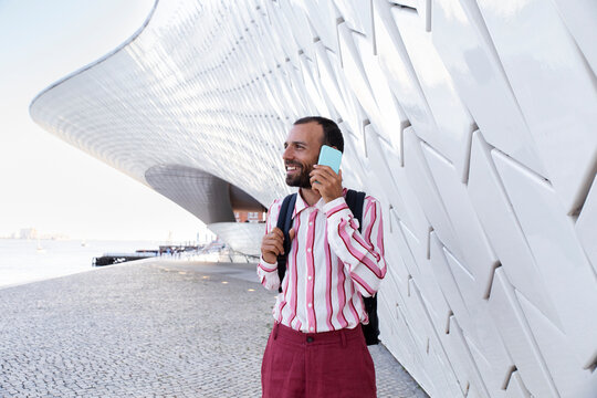 Smiling man with pink shirt using phone near MAAT in Lisbon outdoors