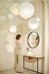 Elegant woman in a shimmering dress stands near a stylish bathroom mirror