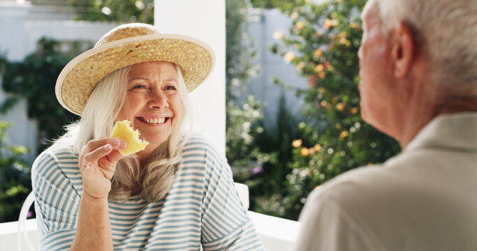 Patio, old couple and break with fruit, home and conversation on weekend, wellness and healthy food. Outdoor, senior woman and elderly man with pineapple on date, romance or people with commitment