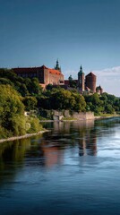 Obraz premium A grand view of Wawel Castle rising above the Vistula River, its Gothic and Renaissance architecture glowing in warm afternoon light