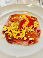 Delicious bresaola served with fried eggs and sautéed bell peppers on a white plate