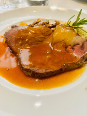 Elegant gourmet main course featuring filet of beef served on a white plate. Tender beef filet slices topped with rich brown gravy, accompanied by vegetables 
